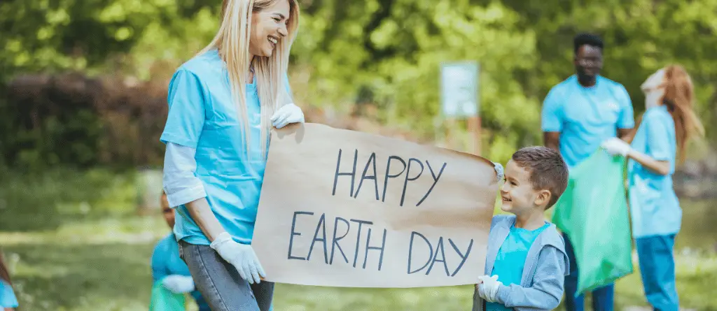 A woman holding a sign reading 'Happy Earth Day' with a young child.