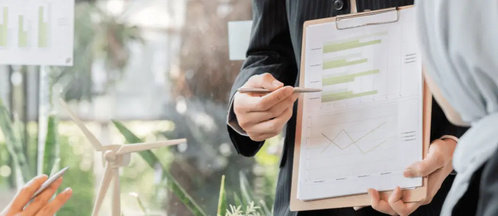 Close up of a business person in a suit showing graphs on a piece of paper, beside a model of a wind generator.