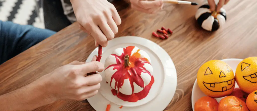 a close-up of a person melting wax crayons over a white pumpkin in order to create an eco-friendly Halloween decoration