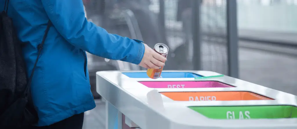 A close-up of somebody putting an aluminium drinks can into a recycling bin.