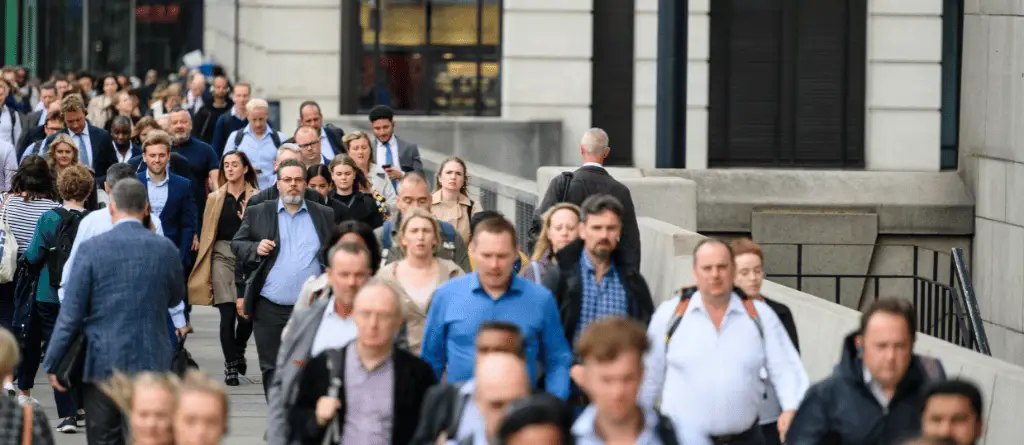 A crowd of people in suits walk through a London street