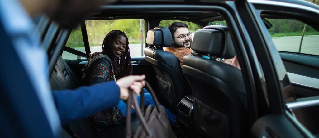 A man in a business suit, entering a car share with a group of people.